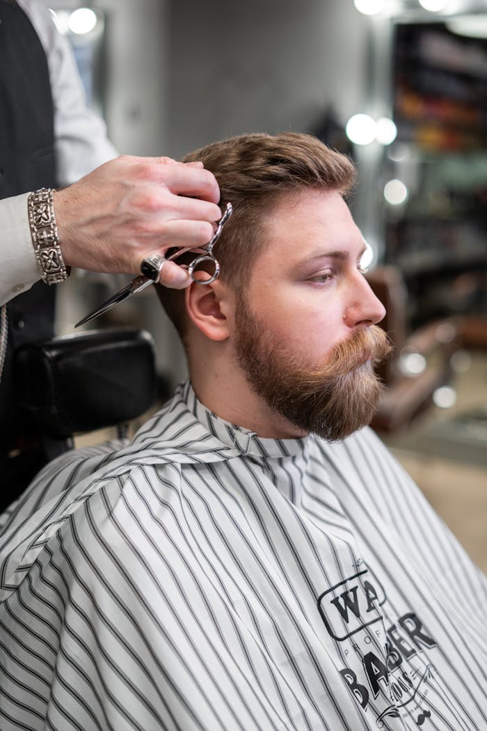 A barber trims a bearded mans hair in a classic barbershop setting.