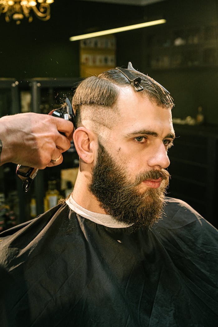 A man receives a haircut and trim in a professional barbershop setting with focus on style and detail.